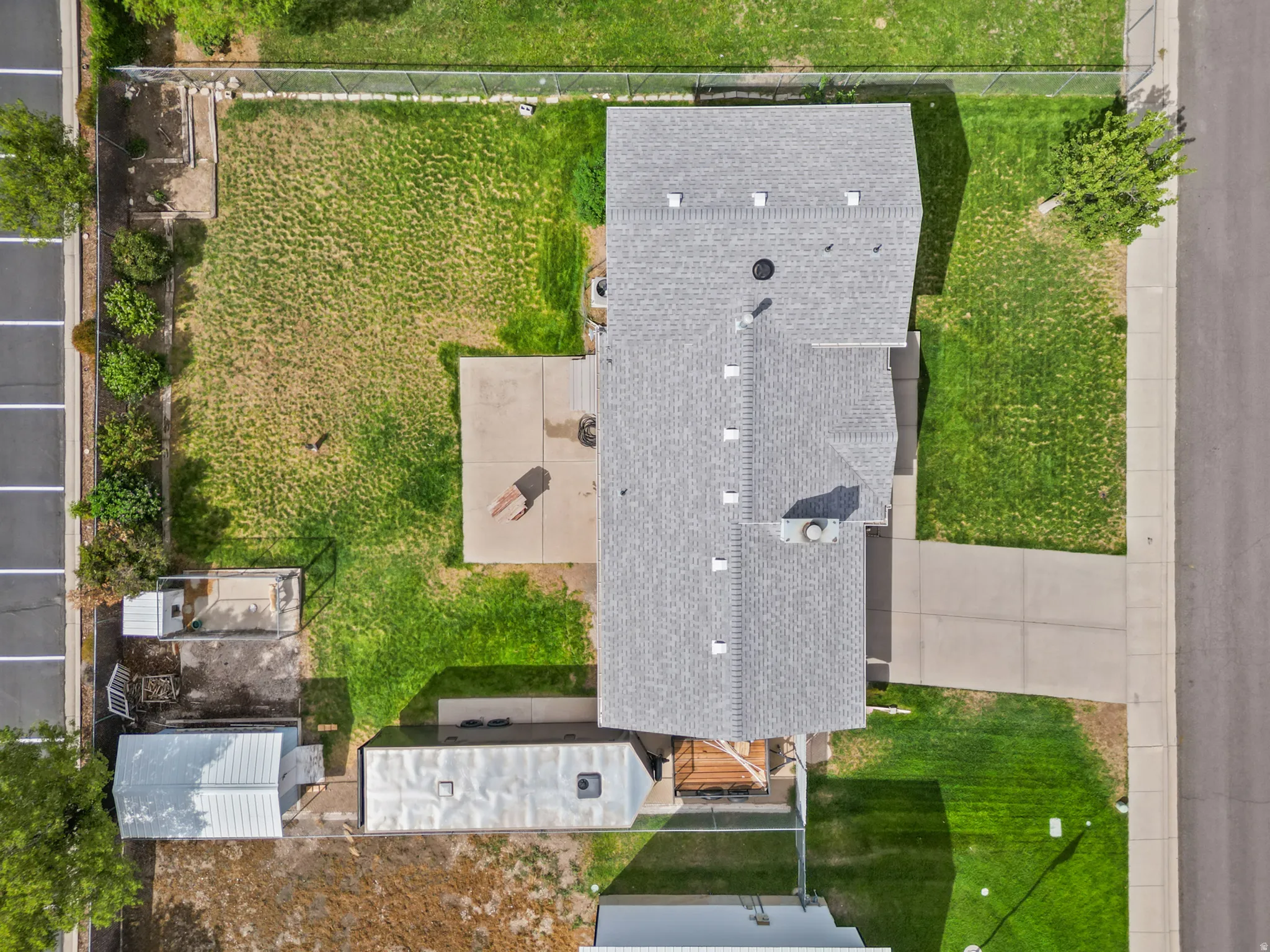 Paved driveway, concrete patio, expansive lawn, mature perimeter landscaping, and a fenced yard