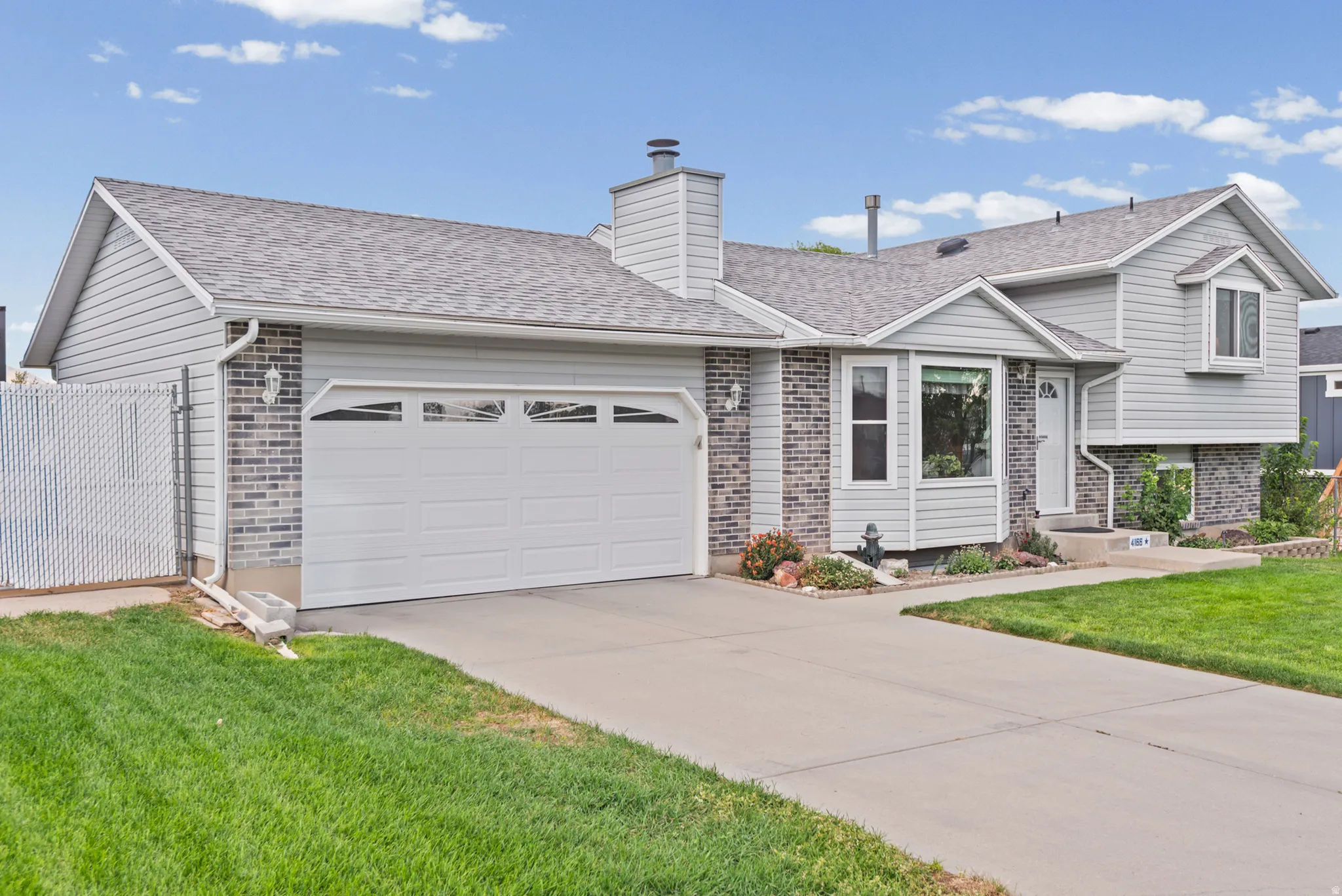 Exterior featuring light grey siding, dark grey brick accents, an attached two-car garage, and a concrete driveway