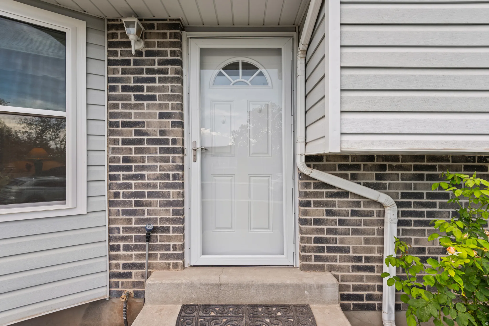 Exterior featuring light gray siding, dark brick facade, and a white entry door with an arched window