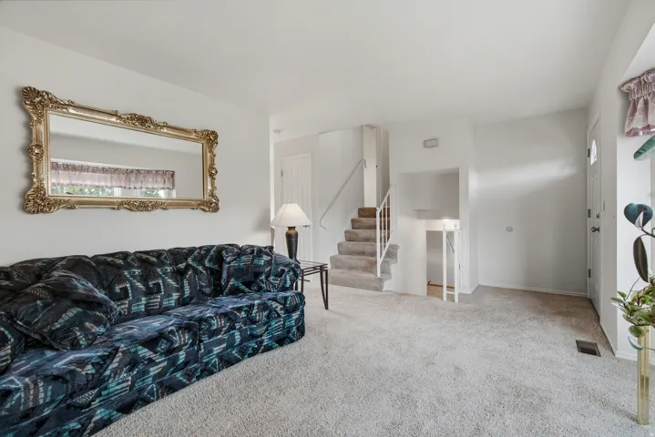Carpeted flooring throughout, white painted walls, and a staircase with a white railing