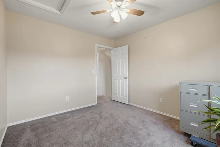 Neutral tone wall paint, textured carpet flooring, ceiling-mounted fan with light fixture, and white trim work