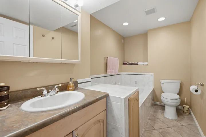 Vanity with integrated sink, medicine cabinet with mirrored doors, tiled jetted bathtub, tiled flooring, and recessed ceiling lighting