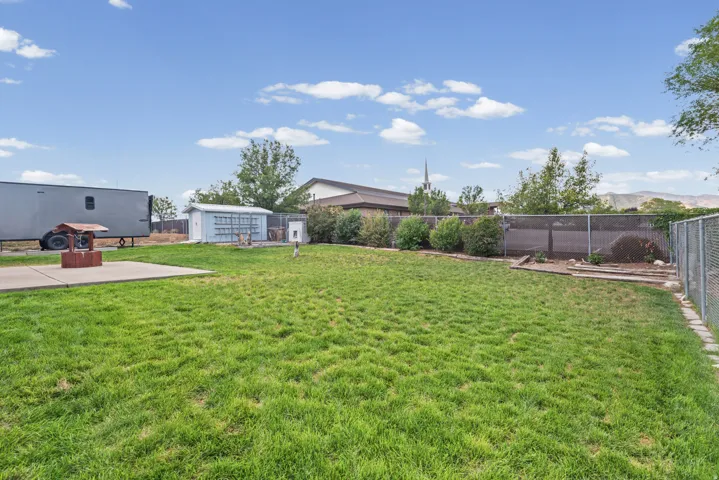 Expansive grass lawn featuring a concrete patio pad, mature shrubs, and a chain link fence