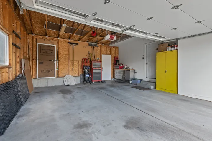 Concrete flooring garage with an overhead door, wood-paneled wall, and a side entry door