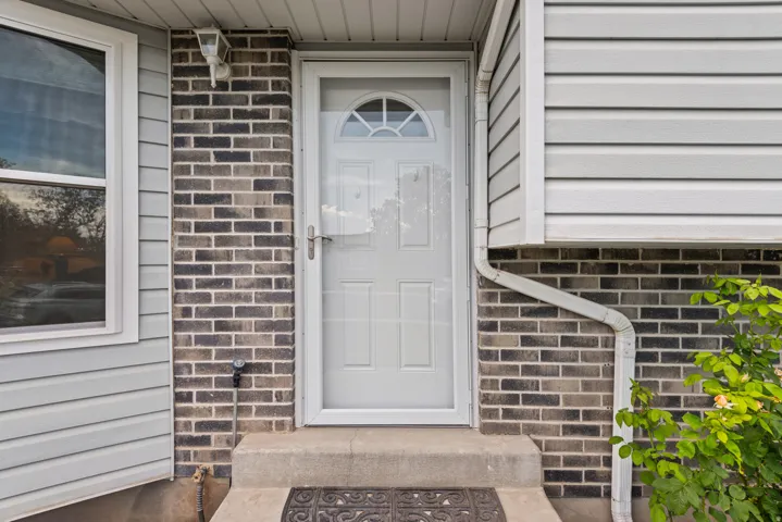 Exterior featuring light gray siding, dark brick facade, and a white entry door with an arched window