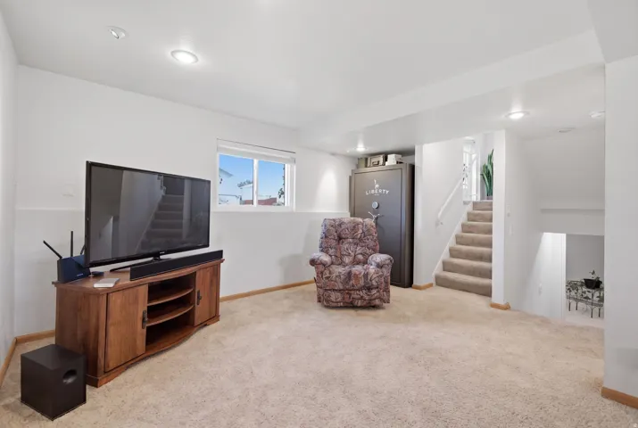 Recessed lighting illuminates this carpeted room with a window, featuring a staircase with carpeted treads and a painted handrail