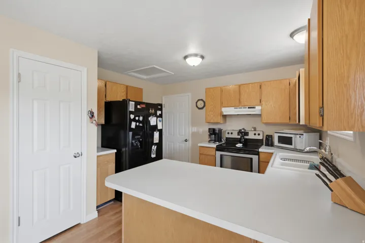 Kitchen featuring light wood-finish cabinetry, white countertops, a stainless steel range, and a white sink