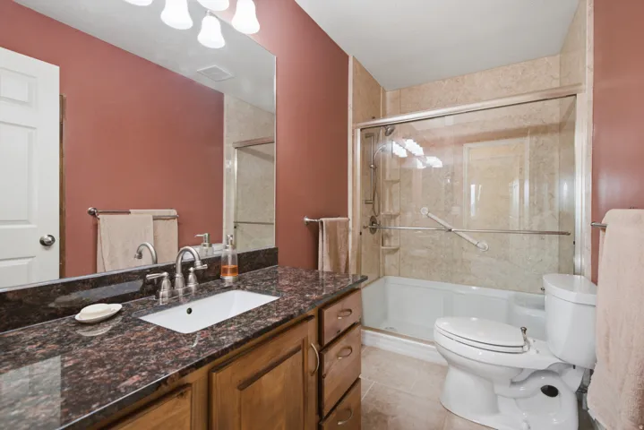 Bathroom featuring a wood-finish vanity with a built-in sink, dark stone countertop, and a shower with a glass enclosure