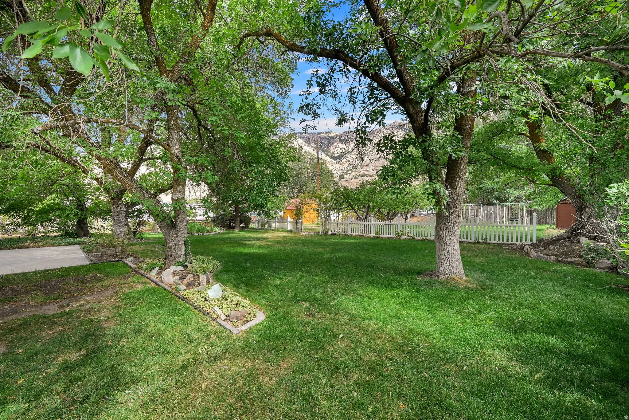 Expansive green lawn framed by mature trees, featuring a white picket fence and a distant mountain backdrop