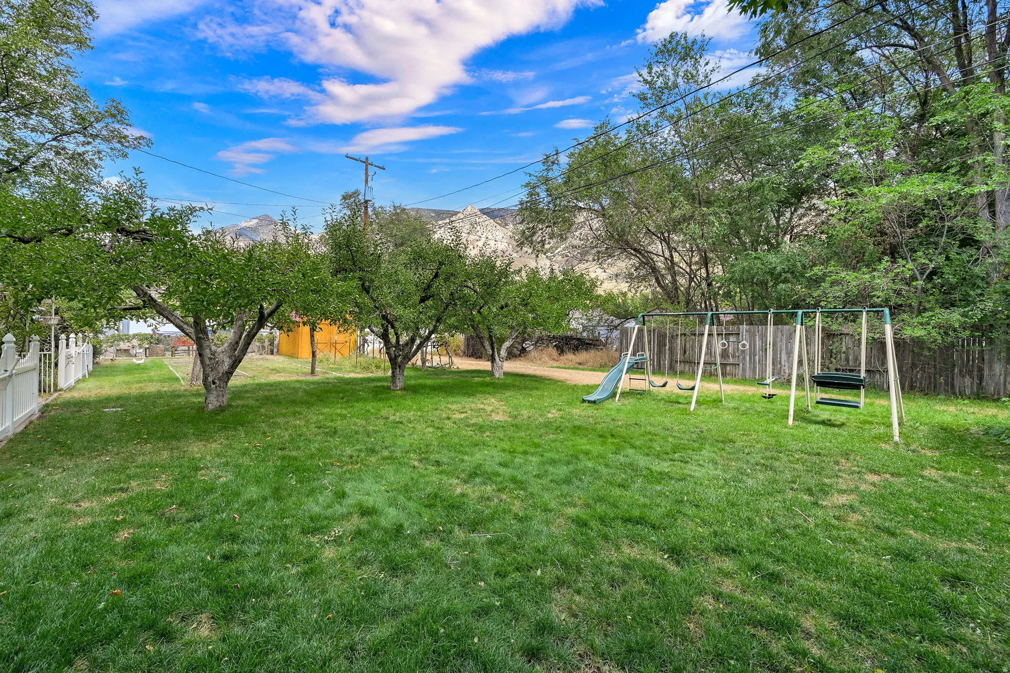 Expansive lawn with mature trees and a white picket fence
