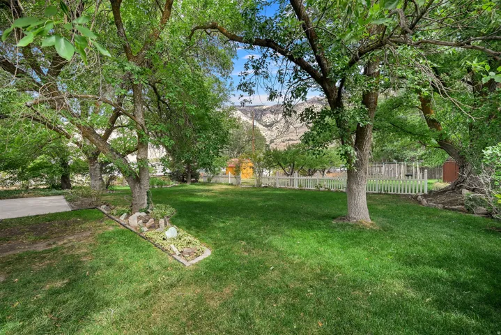 Expansive green lawn framed by mature trees, featuring a white picket fence and a distant mountain backdrop