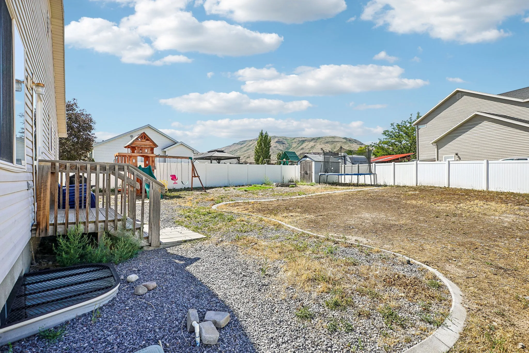 Rear wood deck, full vinyl privacy fencing, gravel ground cover, and a window well