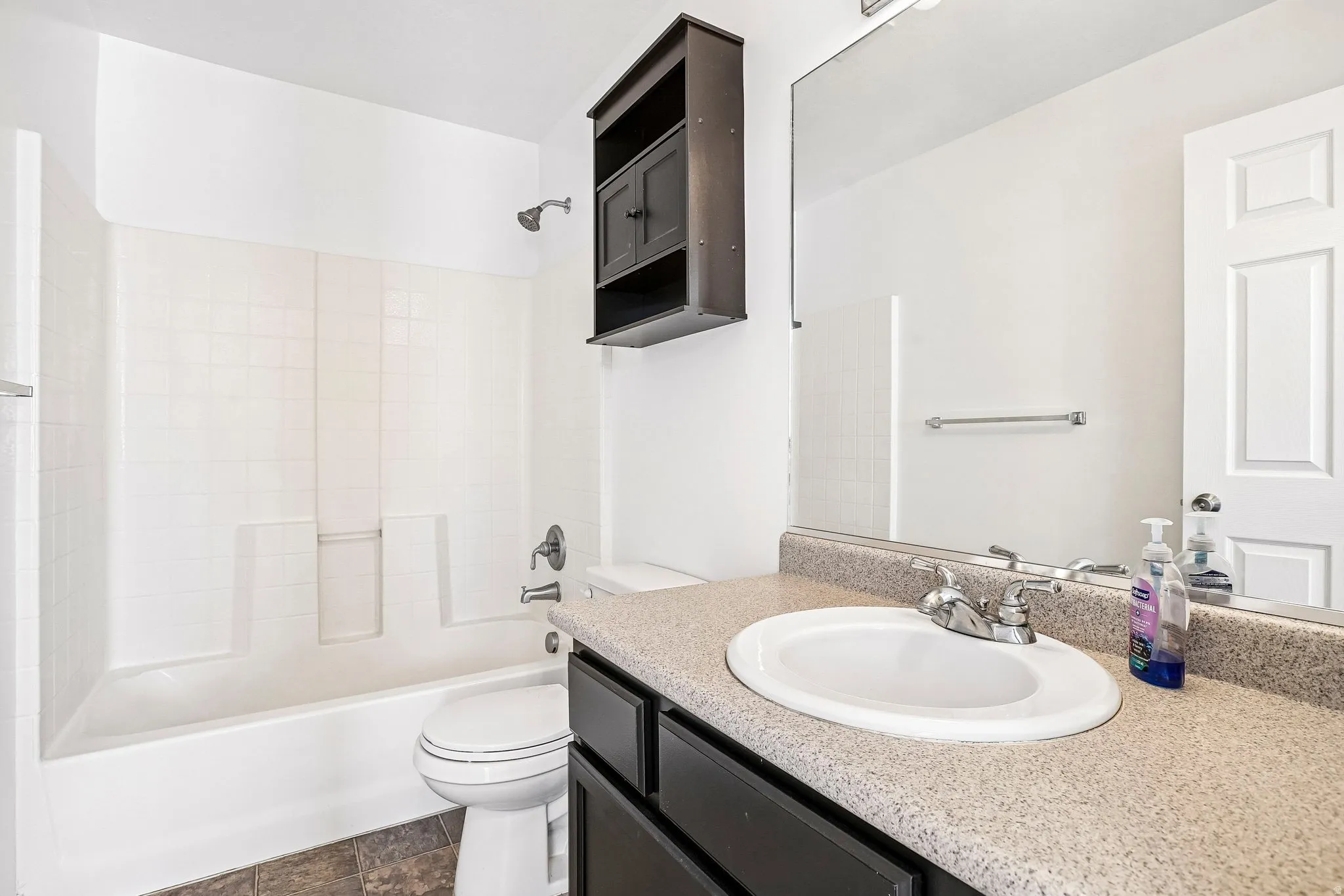 Bathroom featuring a vanity with an integrated sink, a large mirror, a dark wood-finish wall-mounted cabinet, and a white bathtub with a shower