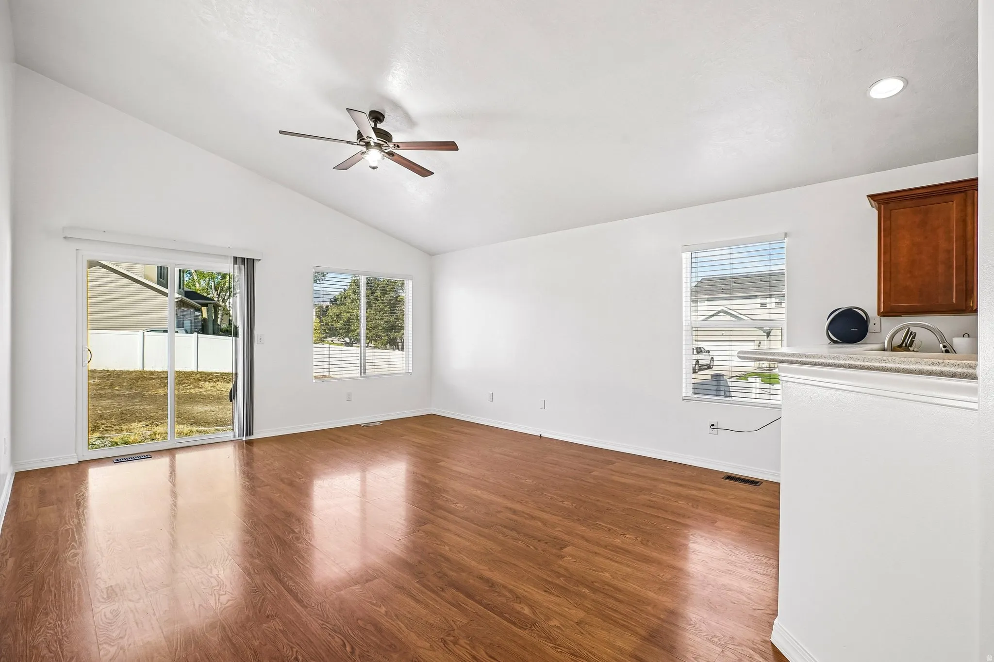 Vaulted ceiling, wood-finish flooring, sliding glass door, multiple windows, and a ceiling fan with light fixture