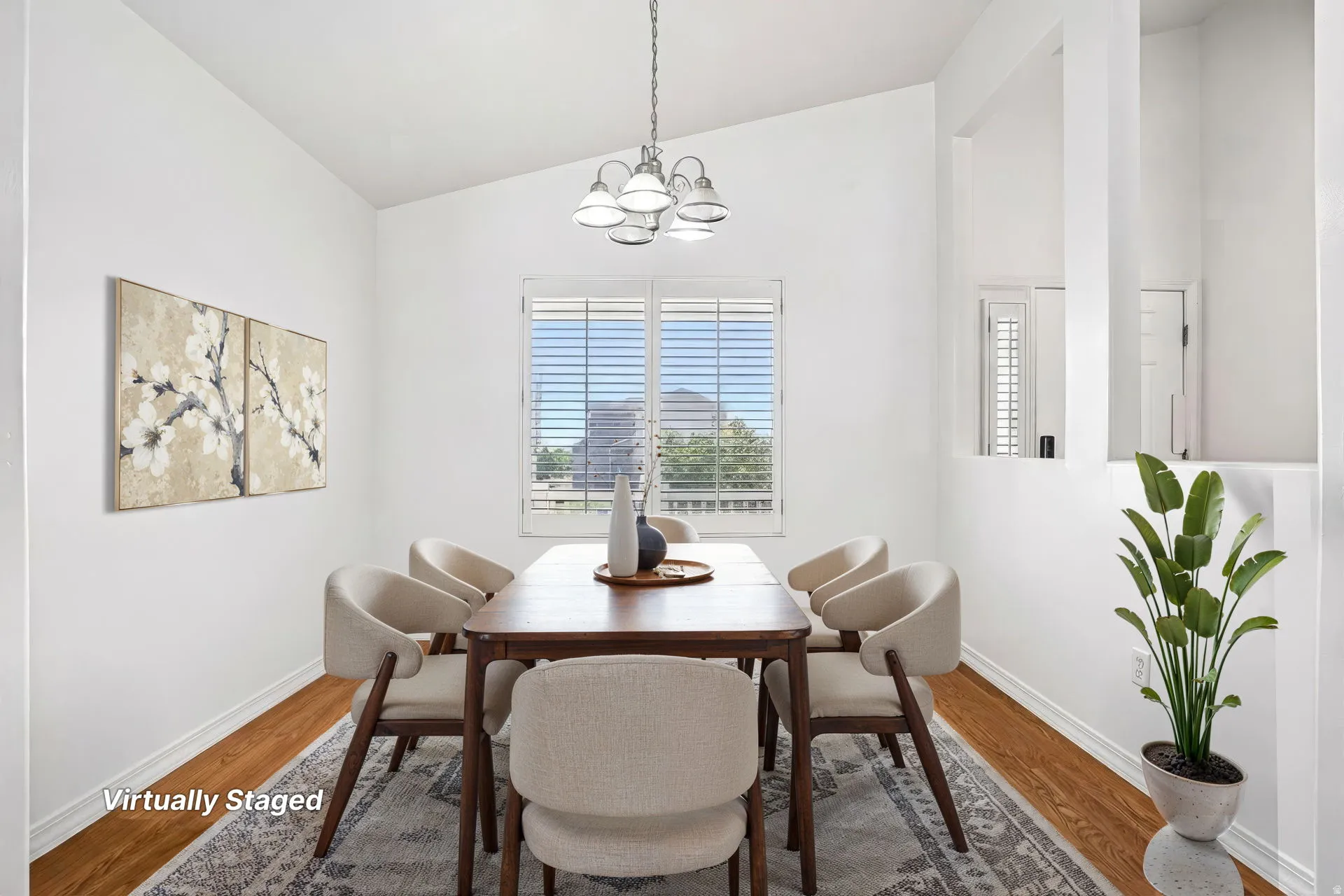 Vaulted ceiling, wood-finish flooring, window with white plantation shutters, decorative wall cutouts, and a chandelier with frosted glass shades
