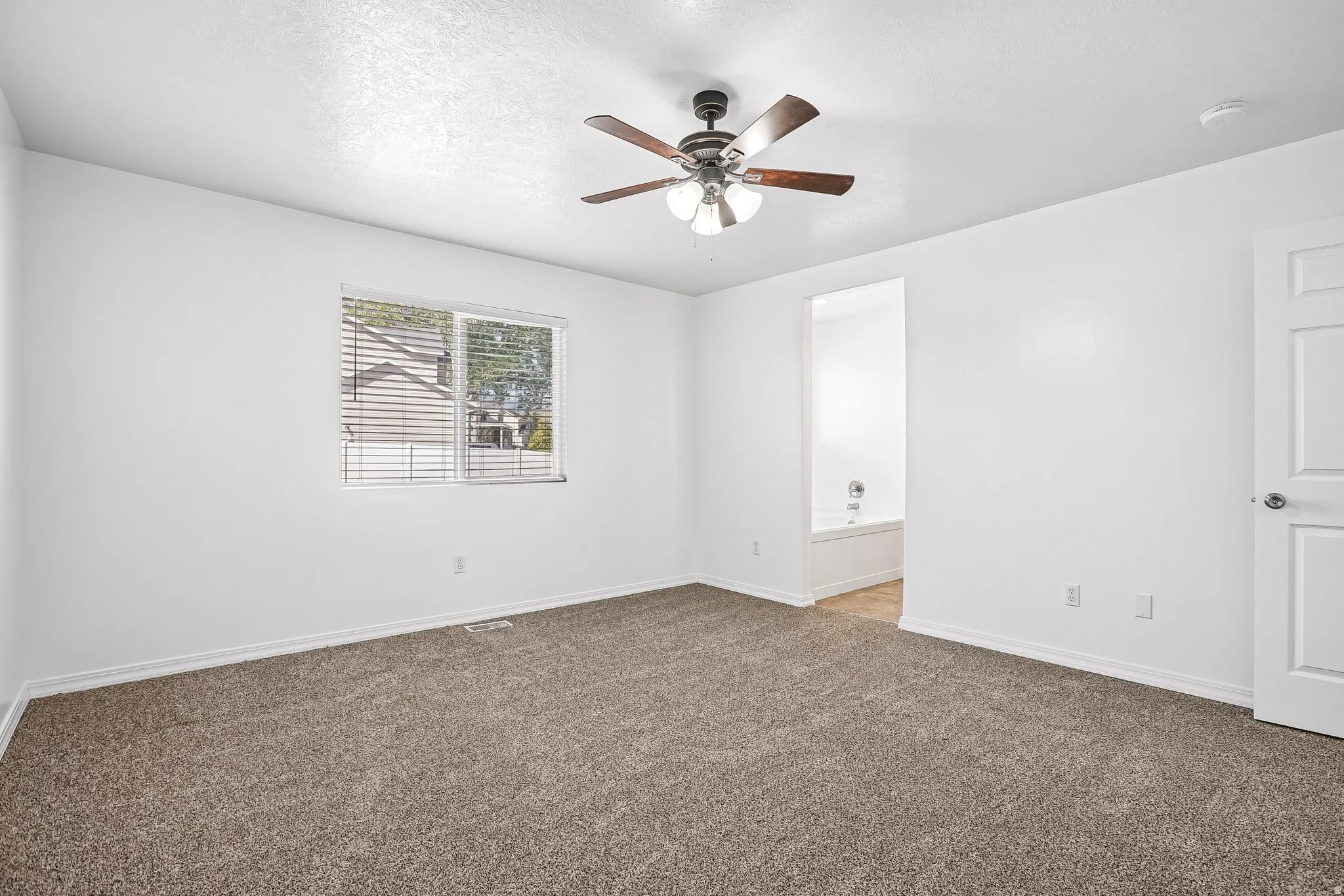 Expansive room featuring carpet flooring, a ceiling fan with integrated lighting, and a window with blinds