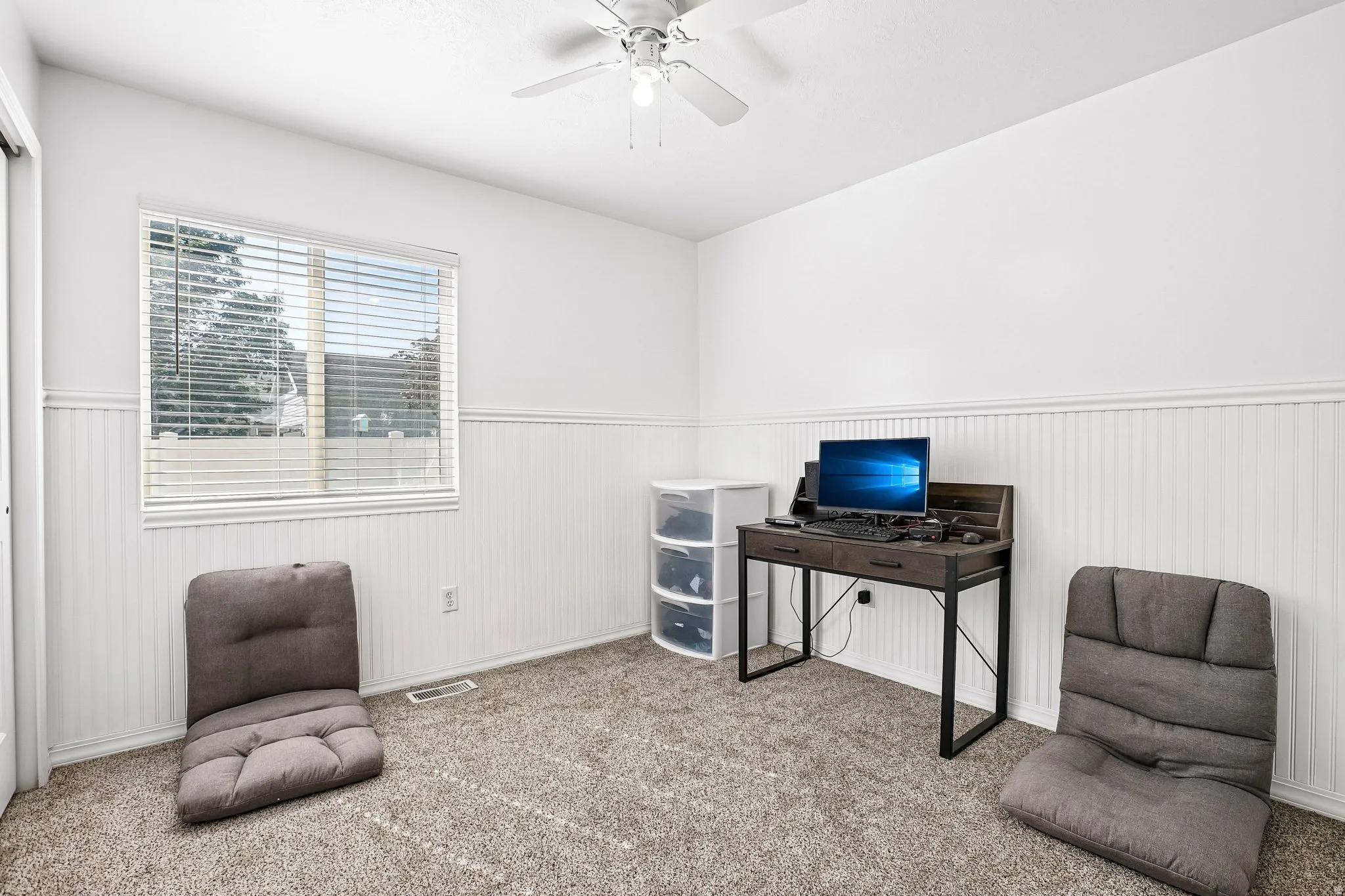 Textured carpet flooring, white beadboard wainscoting, white window blinds, and a ceiling fan with light fixture