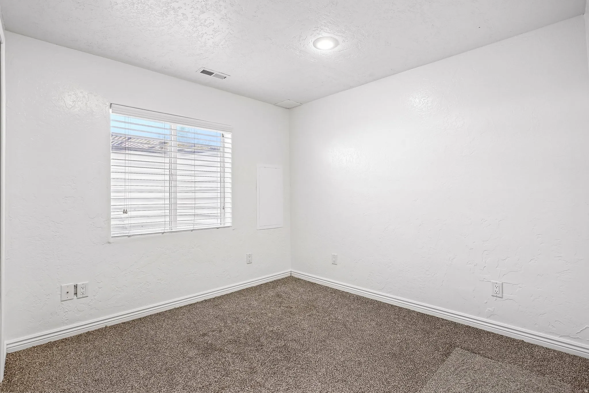Recessed lighting, textured walls, window with blinds, and neutral carpet