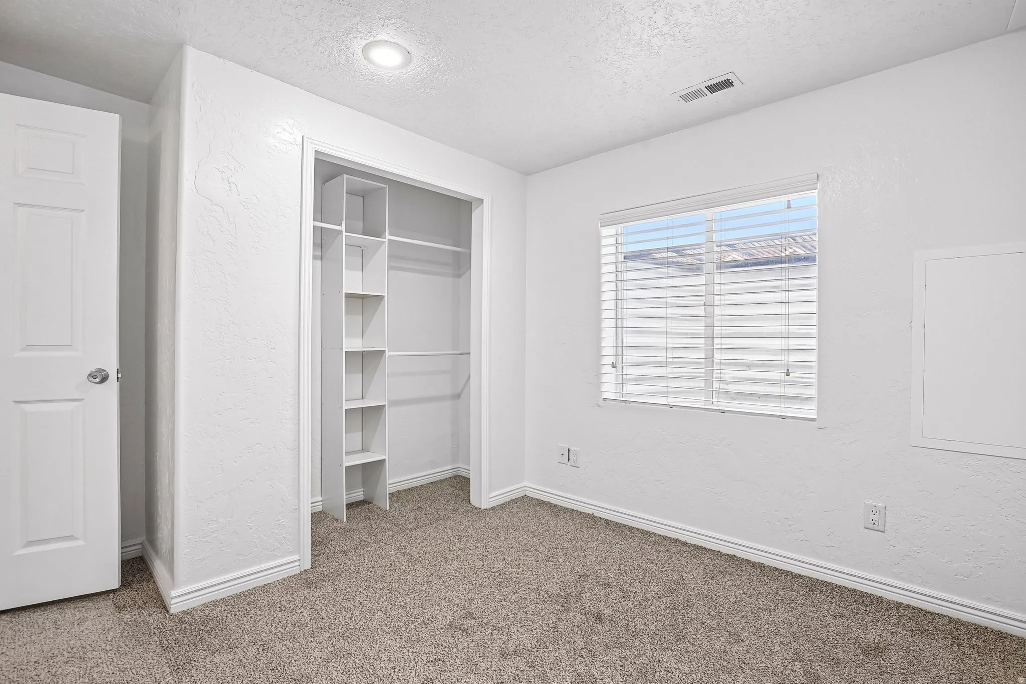 Recessed ceiling lighting, carpet flooring, window with blinds, built-in closet shelving, and a white paneled door
