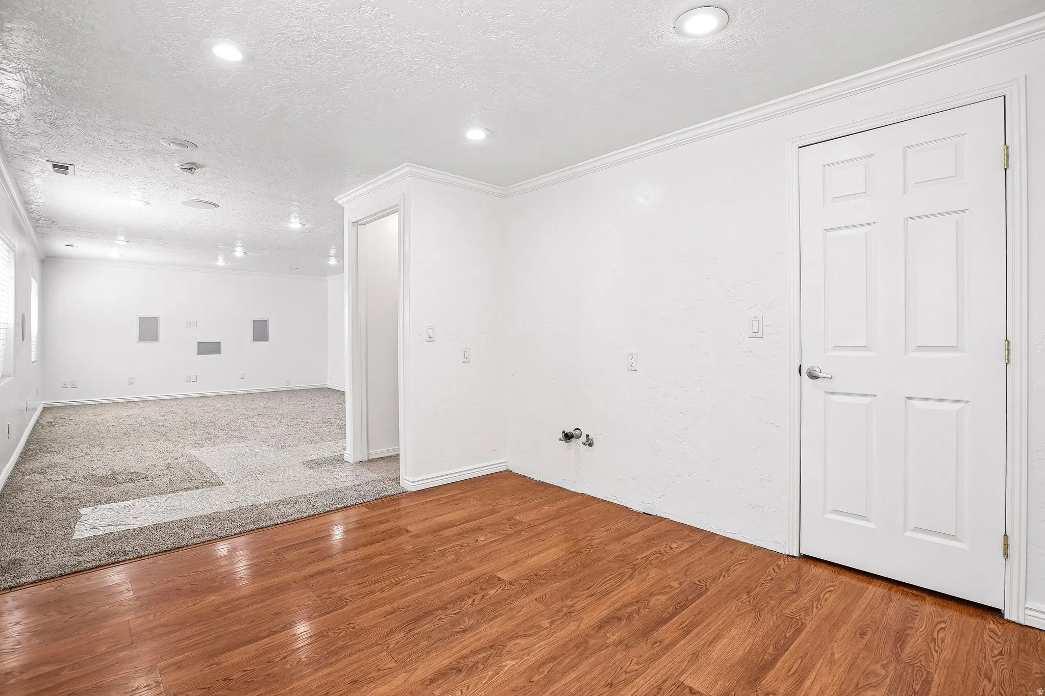 Wood-finish flooring, recessed lighting, white six-panel door, and crown molding