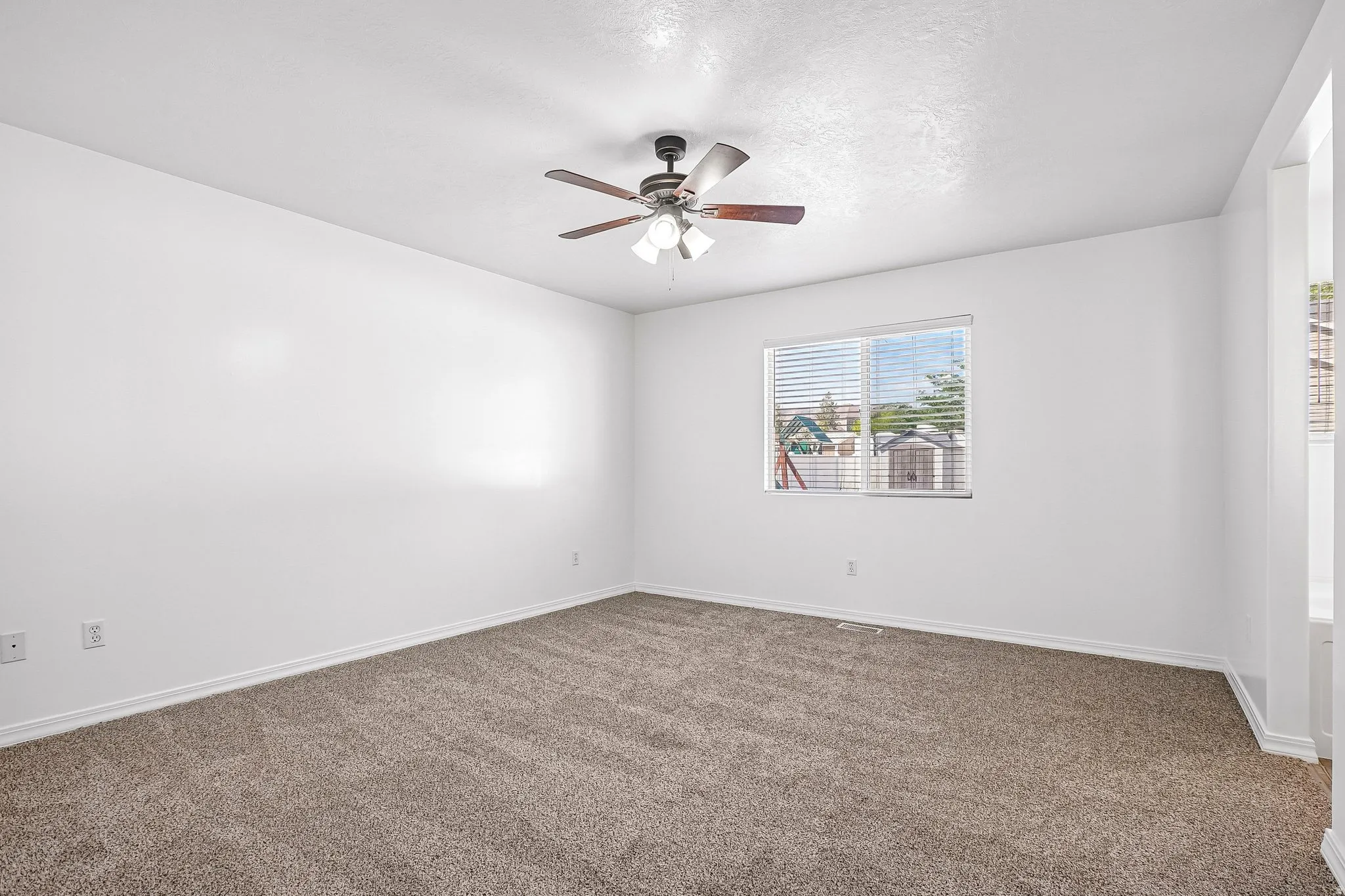 Neutral tone wall paint, carpet flooring, a window with blinds, and a ceiling fan