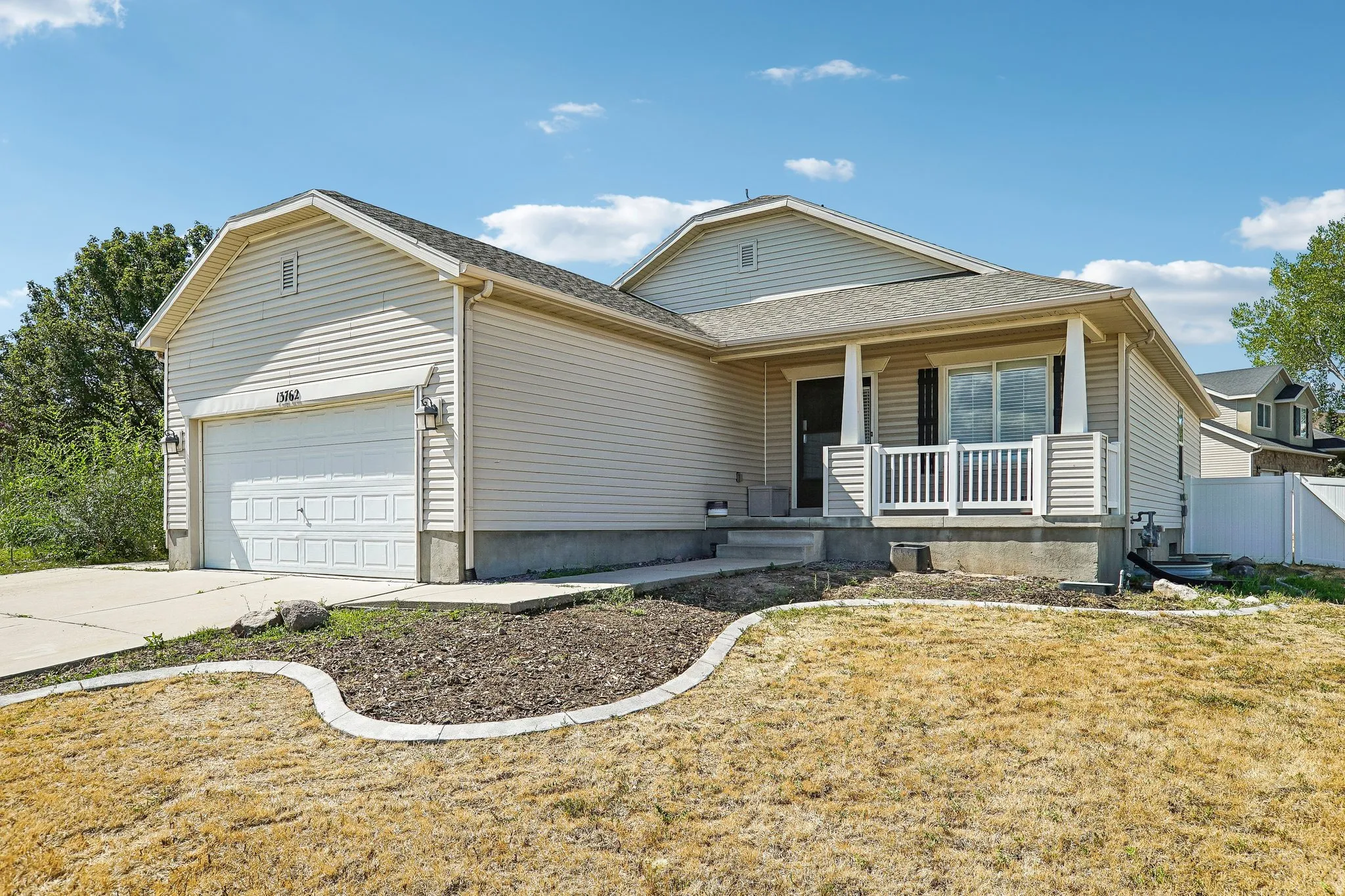 Light-toned siding exterior with a covered porch, white railing, and an attached garage