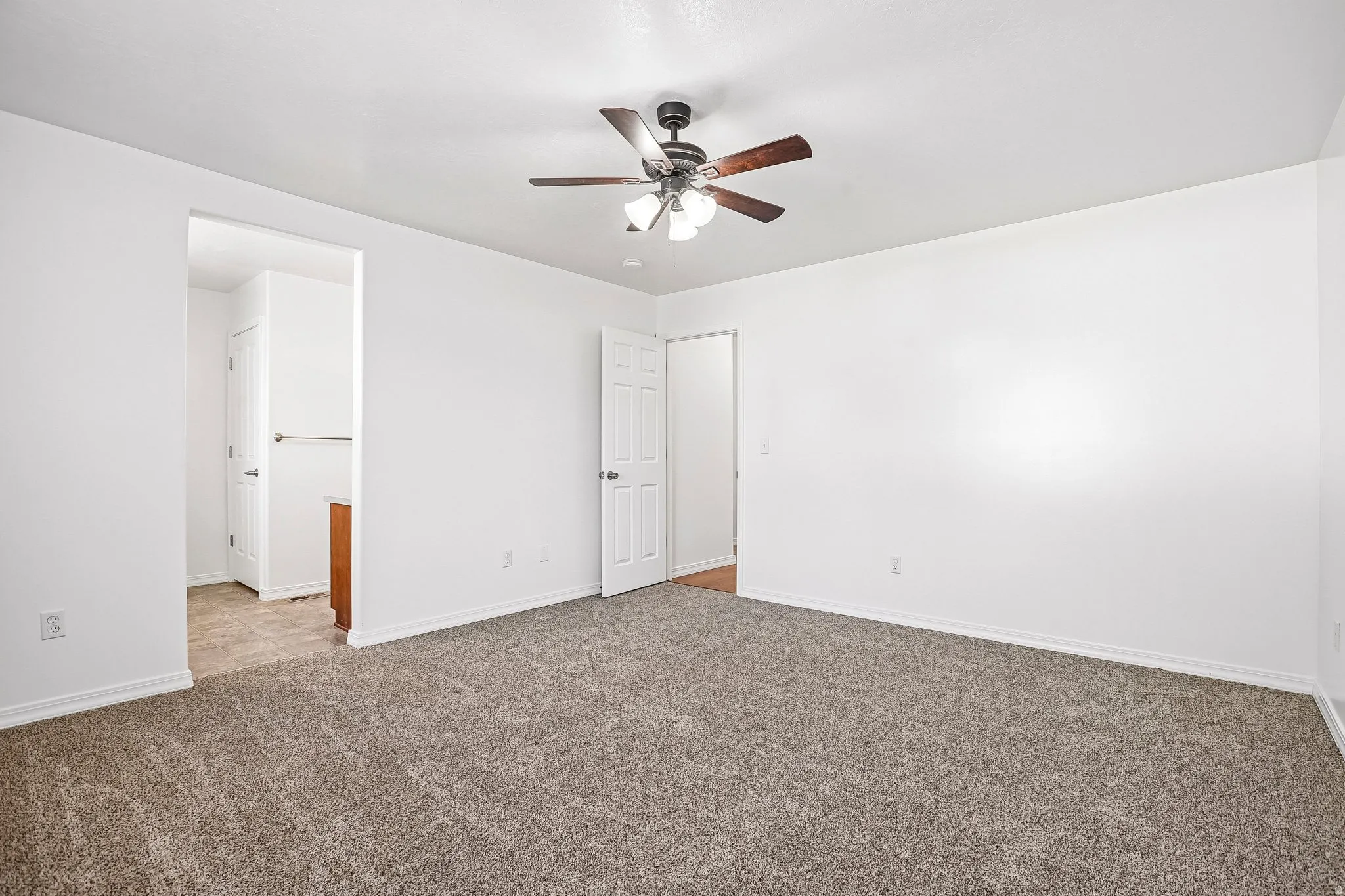 Spacious room featuring neutral carpeting, white walls, and a ceiling fan with integrated lighting