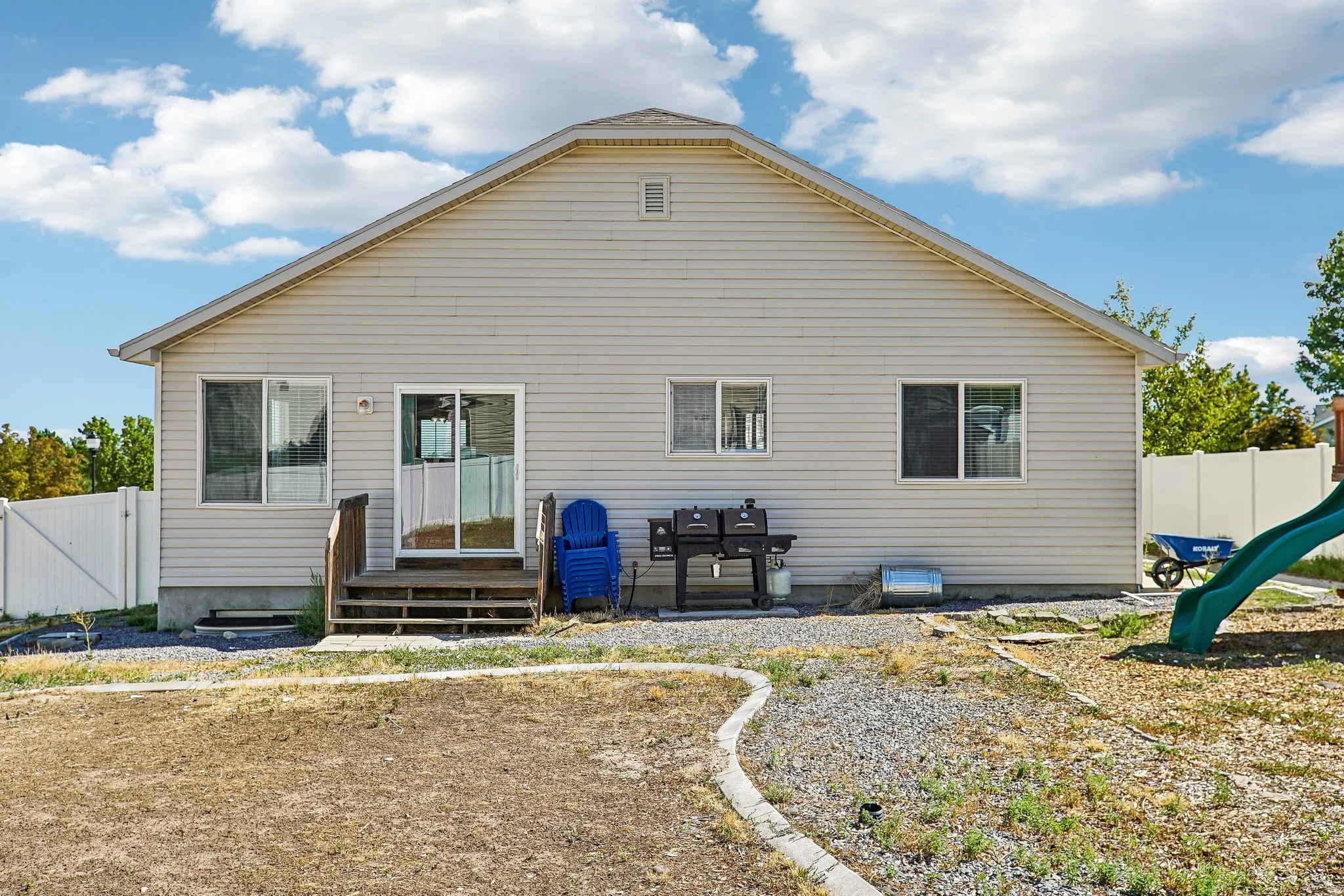Rear exterior with light-colored siding, a gabled roof, and a sliding glass door with a wooden deck