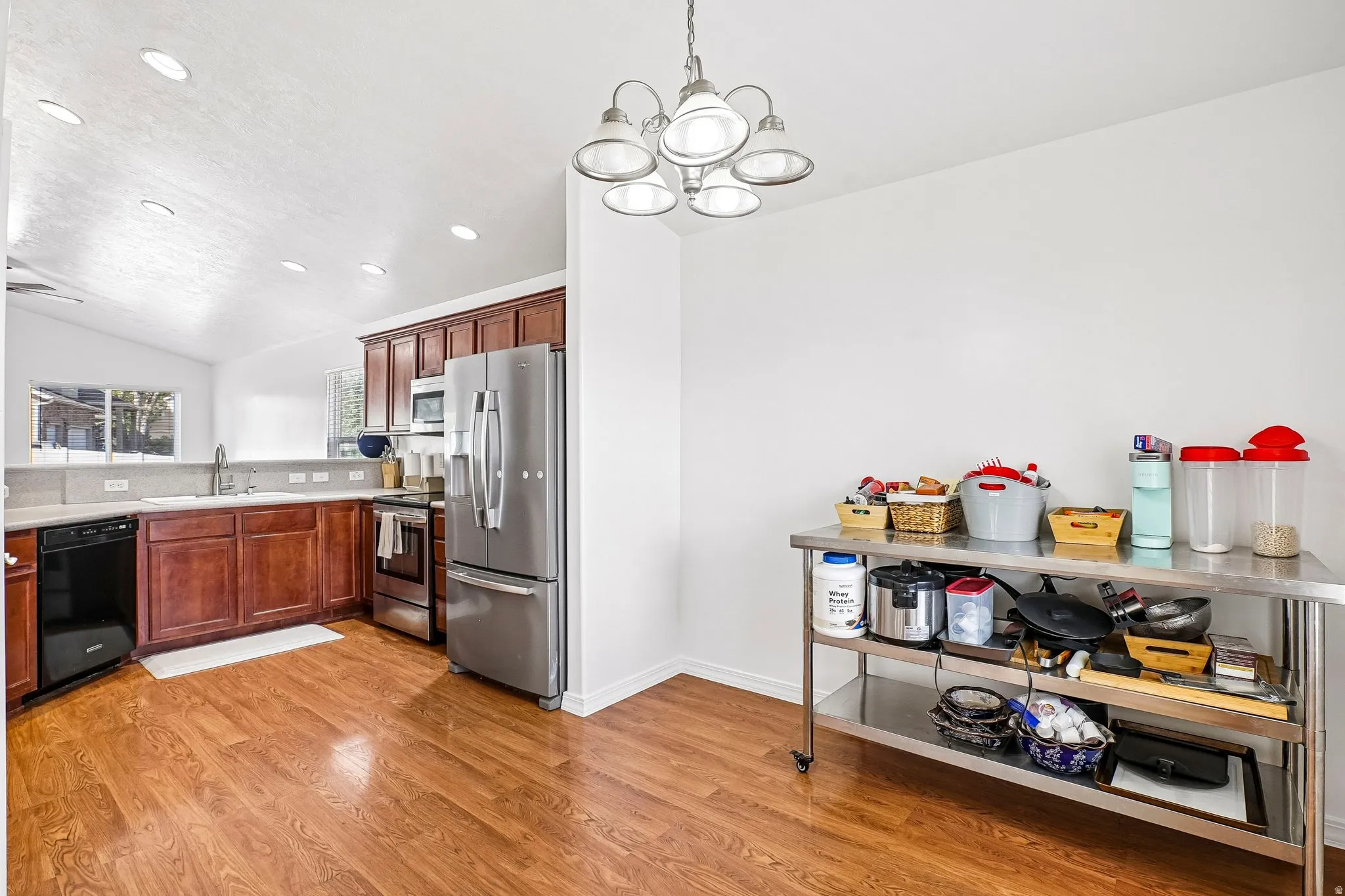 Kitchen featuring wood-finish flooring, dark wood cabinetry, stainless steel appliances, and a vaulted ceiling with recessed lighting