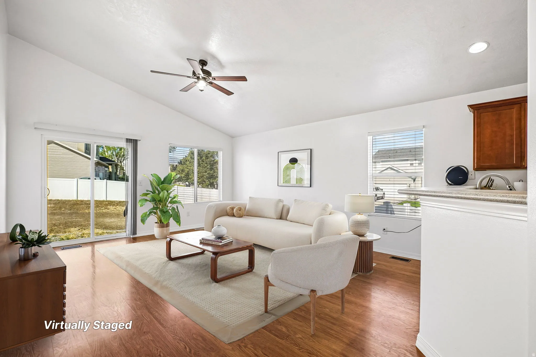 Vaulted ceiling with a ceiling fan, wood-finish flooring, sliding glass door, white window blinds, and a built-in wood-finish cabinet