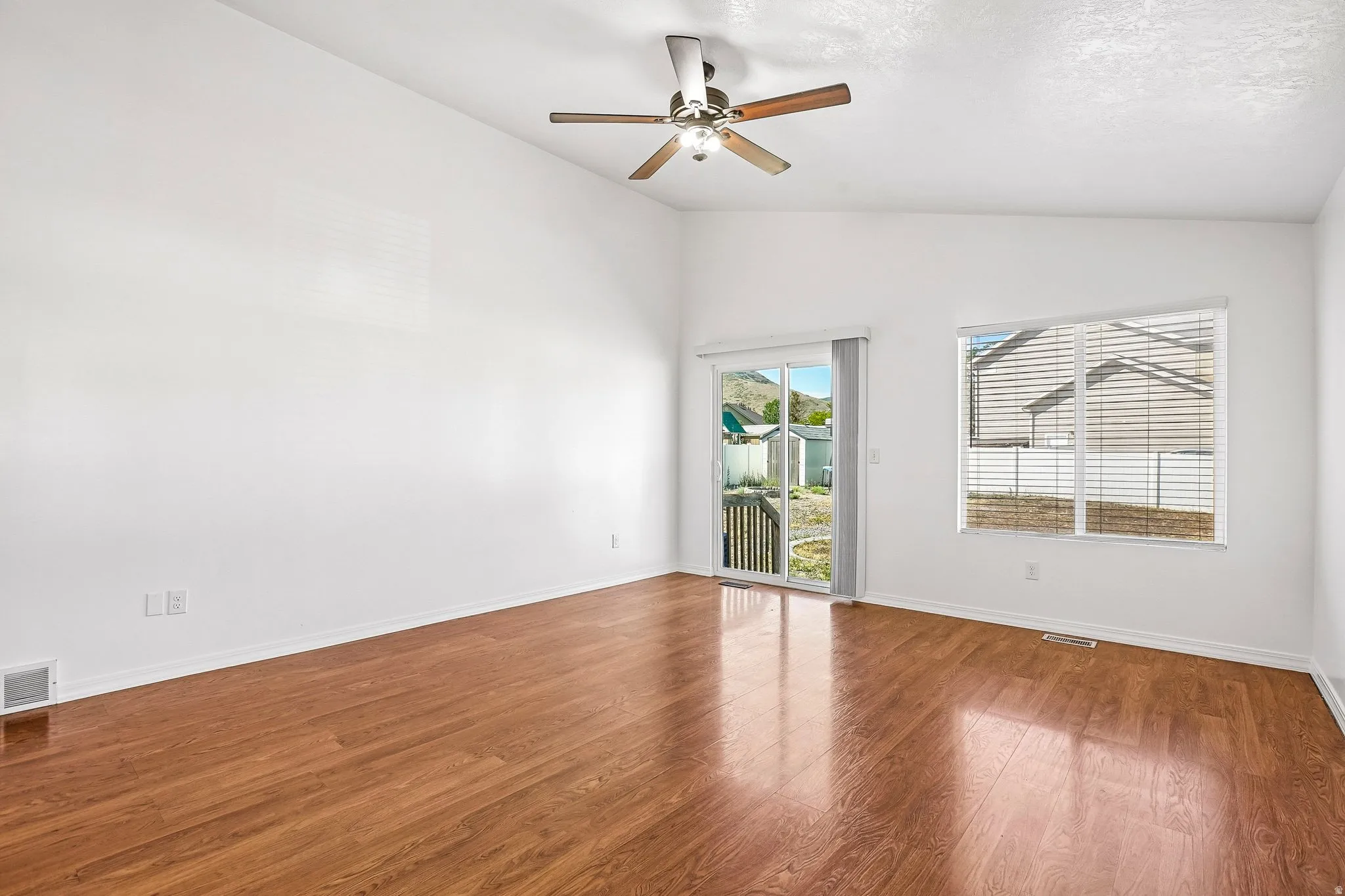 Vaulted ceiling with a ceiling fan, wood-finish flooring, white walls, and a sliding glass door to the exterior