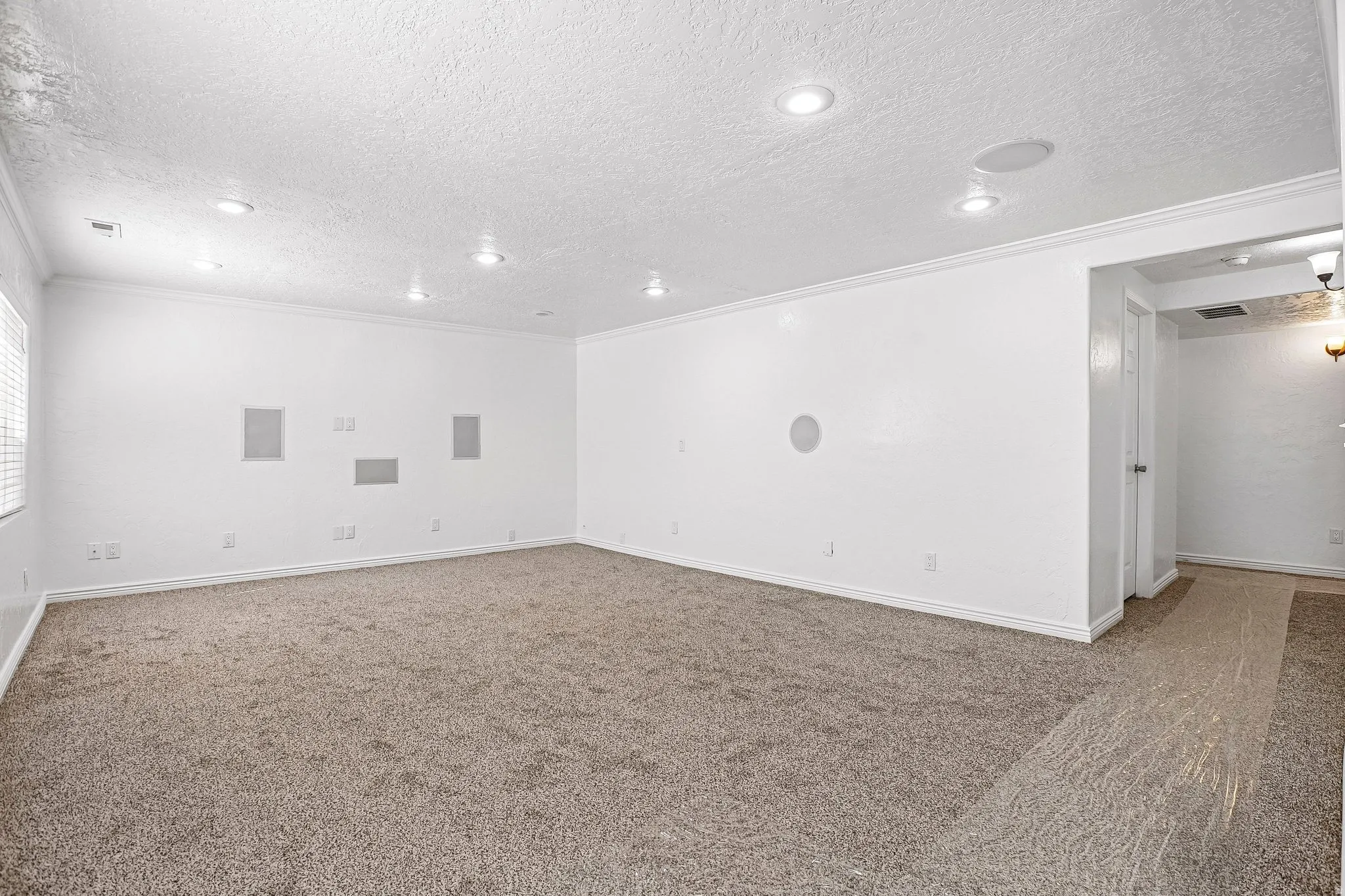 Spacious room with recessed lighting, crown molding, wall-mounted speakers, built-in wall niches, and neutral carpeting