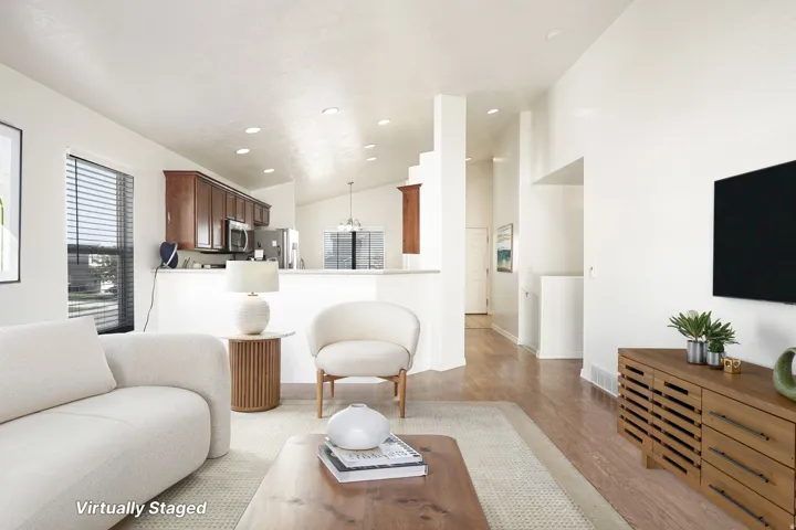 Open-concept living area with vaulted ceilings, wood-finish flooring, recessed lighting, and a kitchen featuring wood cabinetry and stainless steel appliances