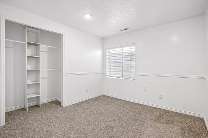 Recessed lighting, built-in closet shelving, window with blinds, wall paneling, and neutral carpeting