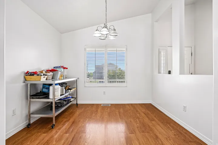 Wood-finish flooring, vaulted ceiling, white interior walls, white window blinds, and an overhead light fixture