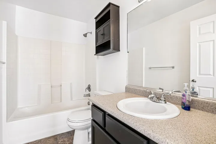 Bathroom featuring a vanity with an integrated sink, a large mirror, a dark wood-finish wall-mounted cabinet, and a white bathtub with a shower