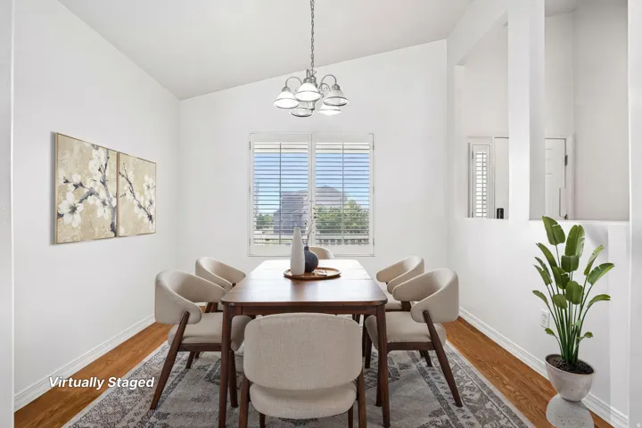 Vaulted ceiling, wood-finish flooring, window with white plantation shutters, decorative wall cutouts, and a chandelier with frosted glass shades