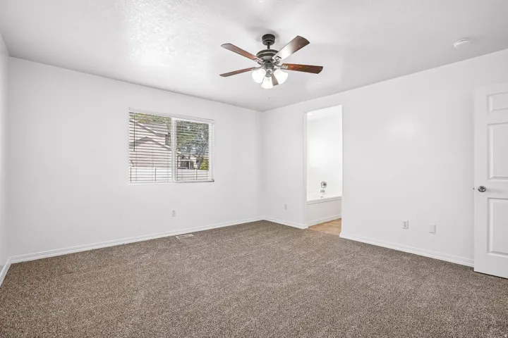 Expansive room featuring carpet flooring, a ceiling fan with integrated lighting, and a window with blinds