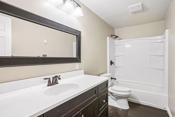 Bathroom featuring a dark wood-finish vanity with a white countertop, an integrated sink, a large framed mirror, and a white tub with a shower fixture