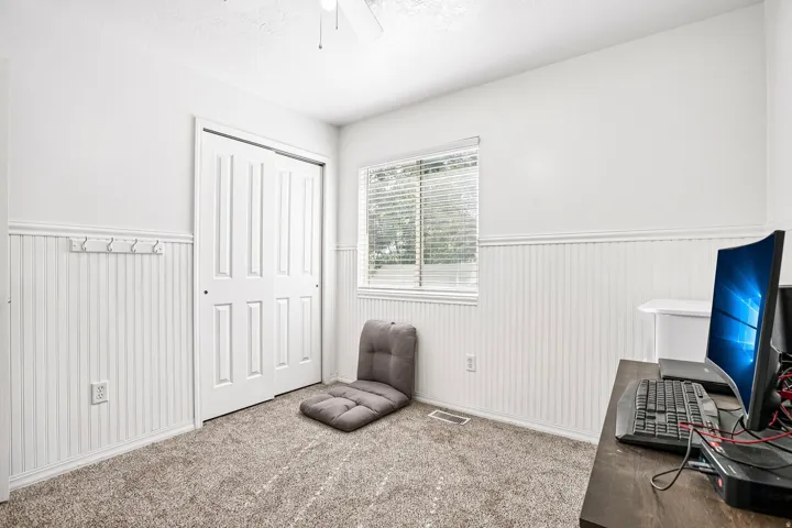 Carpeted flooring, window with blinds, white paneled wainscoting, bi-fold closet doors, and a ceiling fan
