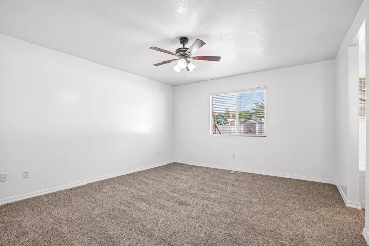 Neutral tone wall paint, carpet flooring, a window with blinds, and a ceiling fan