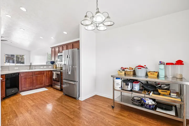 Kitchen featuring wood-finish flooring, dark wood cabinetry, stainless steel appliances, and a vaulted ceiling with recessed lighting
