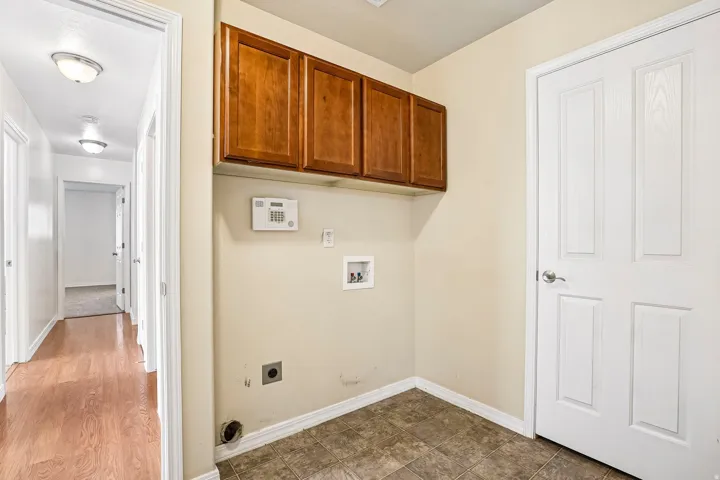Laundry area featuring upper wood-finish cabinetry, a utility sink connection, and durable tile flooring