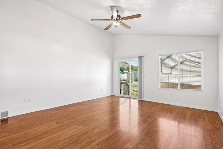 Vaulted ceiling with a ceiling fan, wood-finish flooring, white walls, and a sliding glass door to the exterior