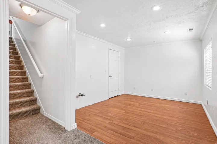 Wood-finish flooring, recessed lighting, crown molding, white trim, and a window with blinds
