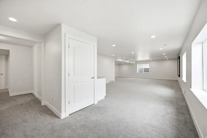 Expansive carpeted area with recessed lighting and multiple windows providing natural illumination