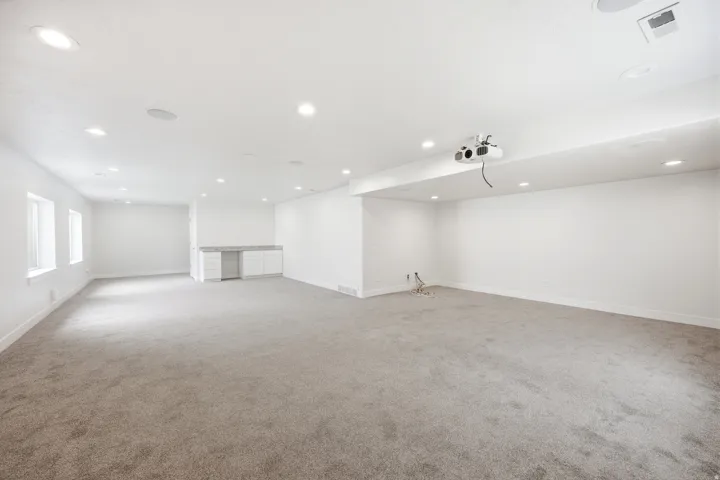 Expansive open-concept room featuring recessed lighting, a built-in projector, a built-in wet bar with white cabinetry, and light gray carpeting