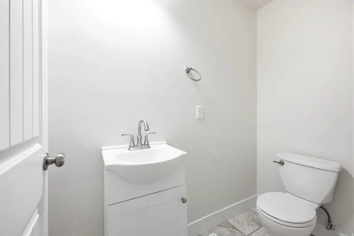 White door with brushed nickel hardware, white vanity with integrated sink, chrome-finish faucet, and tile flooring