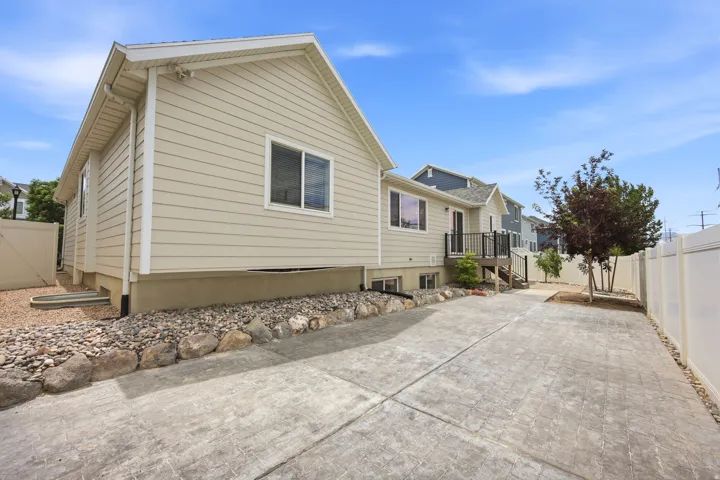 Rear exterior featuring light-toned siding, a stamped concrete patio, a privacy fence, and rock landscaping
