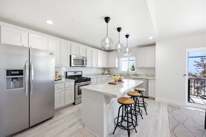White shaker cabinetry with stainless steel appliances, light-toned wood-finish flooring, and a central island featuring pendant lighting